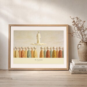 Leaning frame mockup of The Ascension on a rustic wood console beside stacked art books and a tall ceramic vessel with dried stems. The print shows Christ standing in light above a soft cloud while gathered witnesses look upward. The oak frame, broad cream mat, plaster wall, and soft side light create a relaxed display while keeping the title and Acts 1:9 legible.