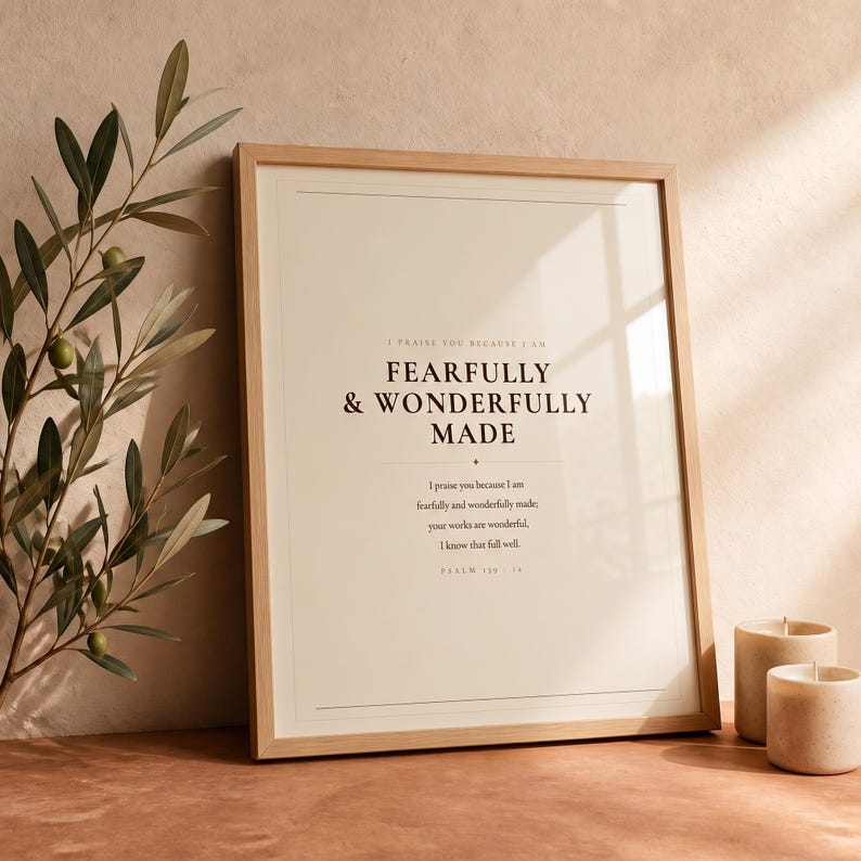 Botanical glass frame scene with the artwork near leafy stems, gentle reflections, warm wood, and soft natural light. The Fearfully and Wonderfully Made artwork uses minimalist boho typography in beige, brown, and black. This Psalm 139:14 print suits a nursery, baptism gift, baby dedication, bedroom, or quiet Christian reading corner as printable digital wall art.