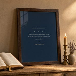 Jeremiah 3:15 scripture print in rustic walnut frame leaning on an oak console beside an open leather Bible and dried lavender stems in earthenware vase, warm editorial pastoral gifts display, thank you pastor christian wall art digital download, pastor church leader appreciation gift by TheFramedVerse
