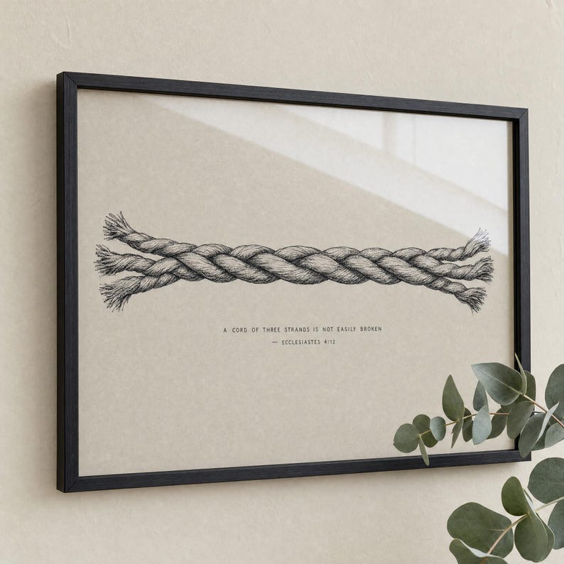 Premium close-up of the Cord of Three Strands frame slightly angled, with a soft eucalyptus sprig in the corner and clear glass reflection across the artwork. Hand-drawn Ecclesiastes 4:12 Christian wedding bible verse wall art, instant digital download.