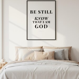 Psalm 46 10 Wall Art Be Still and Know That I Am God Scripture Print Christian, — "Be still and know that I am God. I will be exalted among the nations", in contemporary bold serif typography in black on clean white background, photographed in beautiful close-up detail showing the premium glass frame reflection, the crisp typography and the intricate artistic details of the design
