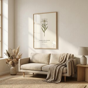 Matthew 6:28 consider the lilies of the field bible verse wall art in oak glass frame above beige linen sofa in scandinavian living room. Vintage lily botanical scripture print with window light reflection. Part of wildflower bible verse wall art set