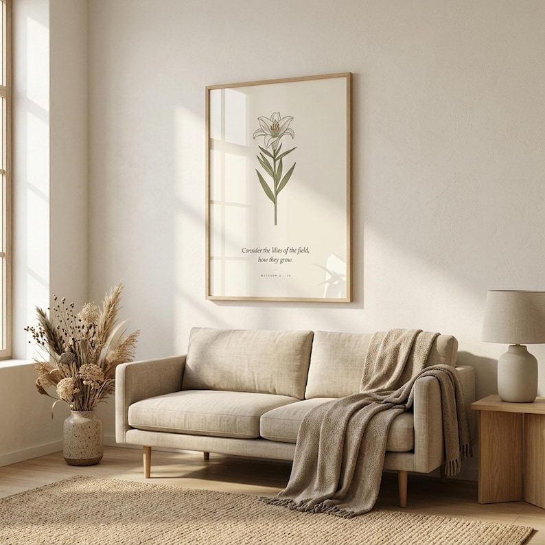 Matthew 6:28 consider the lilies of the field bible verse wall art in oak glass frame above beige linen sofa in scandinavian living room. Vintage lily botanical scripture print with window light reflection. Part of wildflower bible verse wall art set