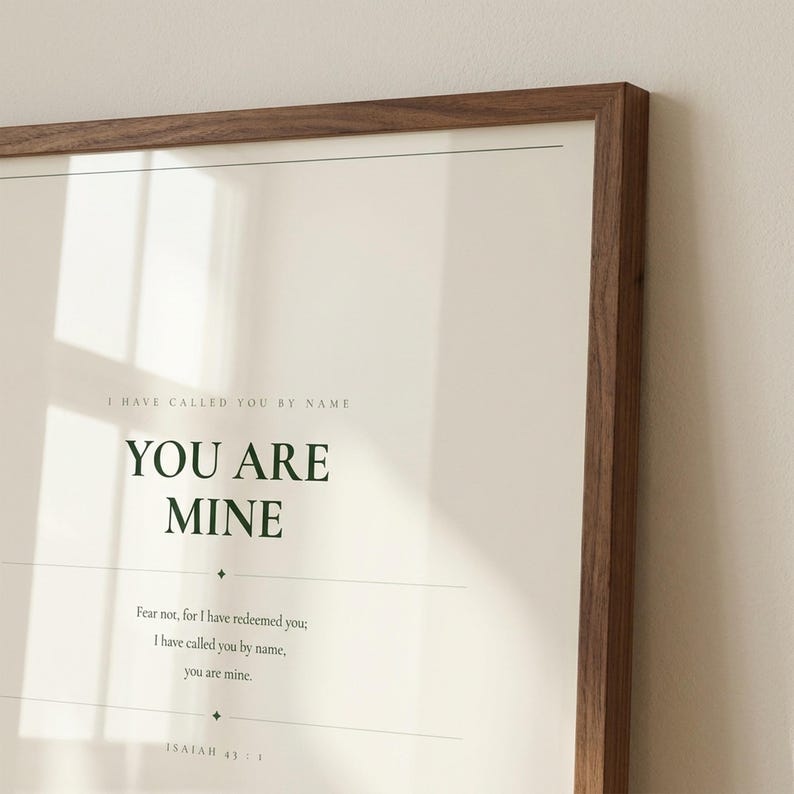 You Are Mine Isaiah 43:1 scripture print minimalist christian baptism gift baby dedication nursery wall art dark forest green typography on warm cream background, close-up detail walnut frame glass reflection natural golden window light cream wall, digital download printable wall art instant download