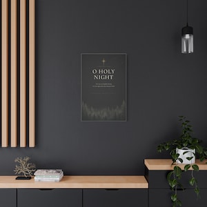 Elegant cream serif lettering spells O Holy Night among glowing golden stars, while shadowy evergreen trees border the textured charcoal paper. The dark black, cream, and gold artwork references the beloved Christmas carol and Luke 2:11 and is printed on stretched canvas. An alternate angle provides a clear product view of the wrapped canvas construction and dramatic vintage design.