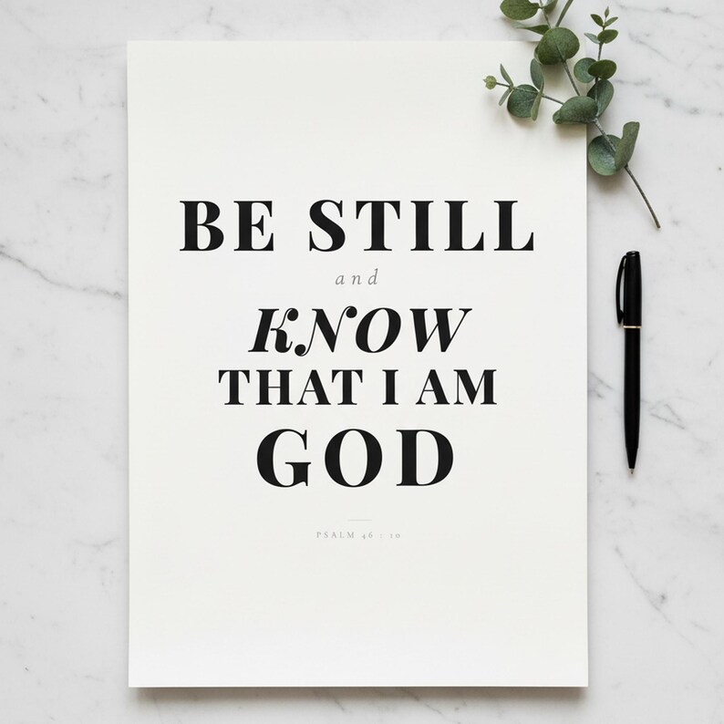 Psalm 46 10 Wall Art Be Still and Know That I Am God Scripture Print Christian, — "Be still and know that I am God. I will be exalted among the nations", in contemporary bold serif typography in black on clean white background, presented as an elegant flat lay on white marble with a fountain pen and eucalyptus sprig, showing the complete print design in full detail
