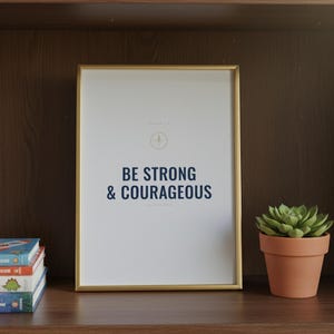 Be Strong and Courageous Joshua 1:9 Wall Art Christian Boys Room Print Scripture — front facing framed mockup on clean white wall with shadow. This elegant christian scripture wall art print features beautiful serif typography on warm cream background. Joshua 1:9 bible verse digital download printable for home office bedroom living room gallery wall decor. Perfect christian gift idea from TheFr...