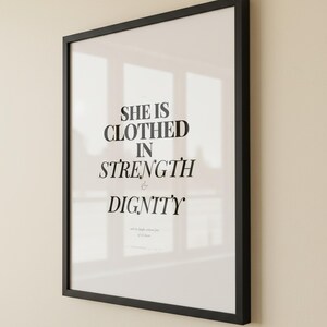 Proverbs 31 25 Wall Art She is Clothed in Strength and Dignity Scripture Print, — "She is clothed with strength and dignity, and she laughs without fear of the future", in elegant Mother's Day design with soft pink watercolor botanical flowers and graceful serif typography, showcased in an elegant contemporary home interior with curated decor elements