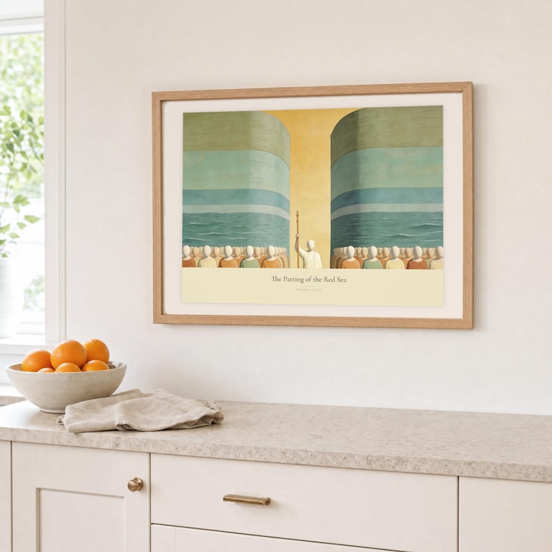 Kitchen mockup of The Parting of the Red Sea framed in light oak above a pale stone counter, white cabinetry, a linen cloth, and a bowl of oranges. The artwork shows Moses on the centre axis between two towering walls of water while the people cross the dry seabed. Bright window light and the warm cream mat demonstrate how the Christian print works in a clean, welcoming kitchen interior.