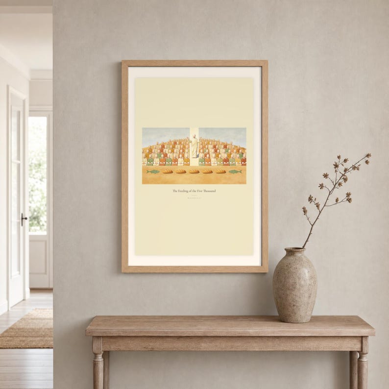 Room mockup of The Feeding of the Five Thousand displayed in a light oak frame on a warm neutral wall. The landscape artwork shows Christ raised on the centre axis above a seated hillside crowd, with loaves and fish laid out along the foreground. A wide cream mat and restrained fresco palette suit a calm living room, prayer space, or Christian home. The printed title and Matthew 14:21 remain visible beneath the image.