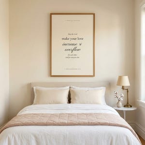 1 Thessalonians 3:12 modern Christian wedding wall art print framed in oak above a cream velvet sofa with linen throw and ivory pillows, side table with ceramic mug and open book, cottage farmhouse Christian newlywed living room, soft afternoon light, digital download from TheFramedVerse Etsy