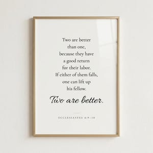 Studio front shot of Ecclesiastes 4:9-10 'Two Are Better Than One' wedding scripture print in refined champagne gold metal frame on soft warm white wall. Editorial product photography — Christian wedding wall art, newlywed gift, first anniversary, engagement present, bridal shower keepsake, instant download.