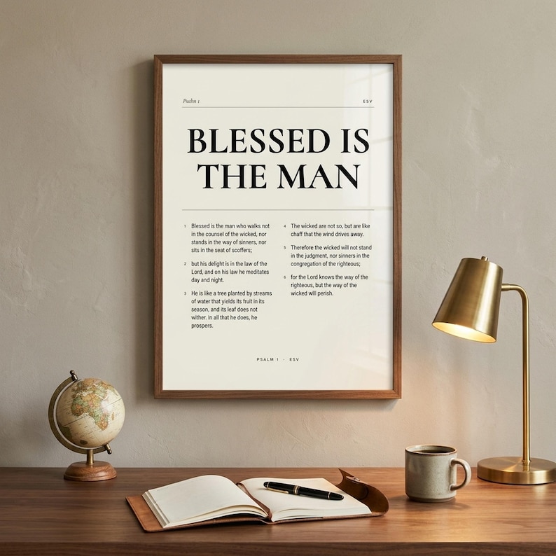 Psalm 1 'Blessed Is The Man' Bible chapter print in walnut wood frame, hanging above a modern Christian home office desk with brass desk lamp, vintage globe, leather notebook, fountain pen, and stoneware mug. Polished masculine Christian home-office aesthetic. Editorial Father's Day digital download from TheFramedVerse on Etsy.