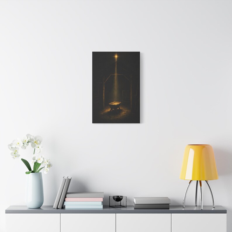 A warm golden beam crosses rough timber, straw, and a humble empty crib beneath the shining Star of Bethlehem. This dark vintage oil painting creates a reverent nighttime manger scene in a rustic stable. Matthew 2:2 nativity wall art in deep brown and gold, printed on stretched canvas. An angled product view shows the gallery wrapped edge clearly.