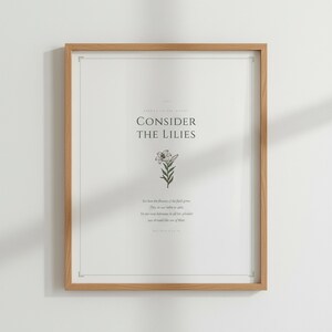 Consider the Lilies Matthew 6:28 sage green botanical scripture art print in thin gold frame, frontal studio shot on cream wall, warm natural daylight from left, elegant bible print minimalist christian style, digital download for gallery wall pairing, TheFramedVerse Etsy shop scripture printable