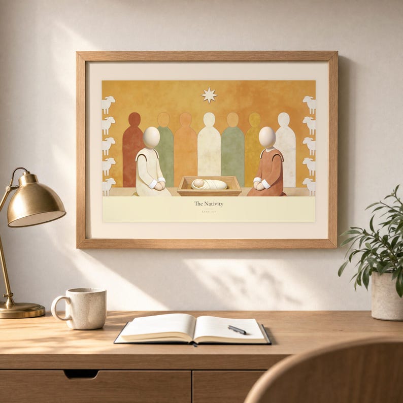 Desk mockup of The Nativity in a light oak frame above a wooden workspace with a brass lamp, ceramic mug, open notebook, pen, and leafy plant. The artwork shows the wrapped child in a low manger between two kneeling figures, beneath a single star. Angled sunlight, neutral styling, and cream matting place the Bible story print in a quiet study or home office setting.