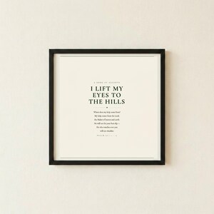 Psalm 121 I Lift My Eyes to the Hills Where Does My Help Come From scripture art print in thin black frame flat mounted on warm cream textured wall, front-facing clean product photo, dark forest green minimalist typography on cream background, christian scripture wall art psalm 121 print baptism housewarming moving gift