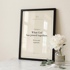 Mark 10:9 'What God Has Joined Together' Christian wedding scripture print in thin black wood frame on white Carrara marble, single olive branch and dried wheat casting soft shadow, two unlit votive candles, warm beige textured wall, bright morning light with clean glass reflection, editorial still life marriage print download from TheFramedVerse