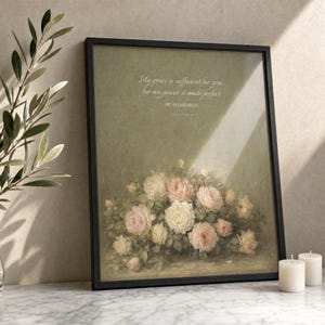 My Grace Is Sufficient 2 Corinthians 12:9 vintage oil painting print in thin black wood frame with visible glass front, leaning at slight angle on white Carrara marble surface, single olive branch casting soft shadow, two unlit votive candles, warm beige textured wall backdrop, bright morning light with clean glass reflection, TheFramedVerse Etsy