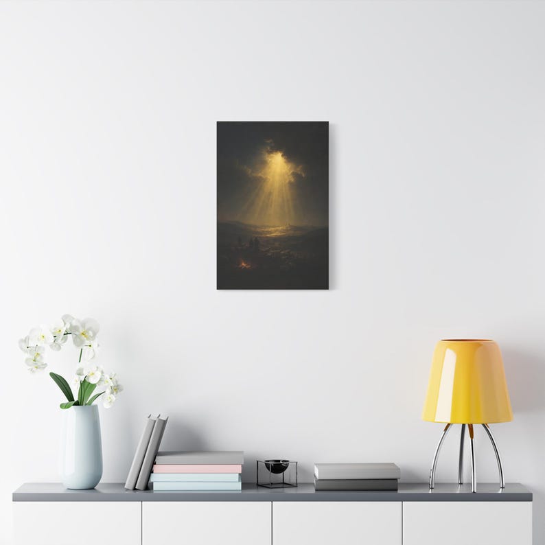 Beside a glowing nighttime campfire, shepherds and their flock gather as heavenly beams cross dramatic clouds over distant Bethlehem. The dark vintage oil painting creates a peaceful and reverent Christmas scene. Luke 2:14 wall art in deep blue, brown, and gold is printed on stretched canvas. This angled product view shows the gallery wrapped edge clearly.
