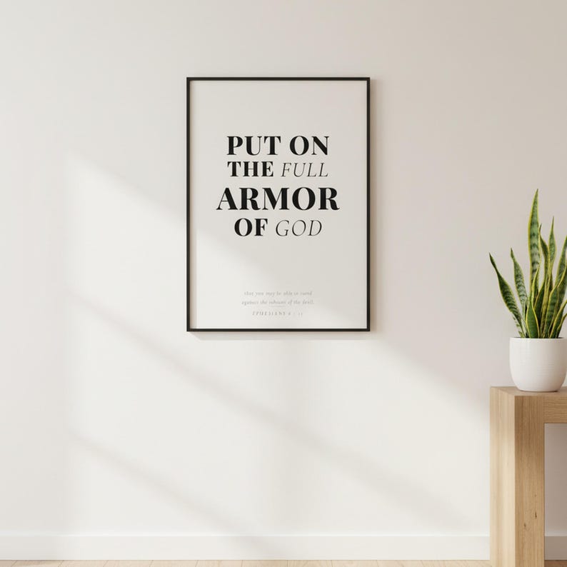 Ephesians 6 Wall Art Put on the Full Armor of God Scripture Print Christian Boys, — "Put on the full armor of God so that you can take your stand against the devil's schemes", in contemporary bold serif typography in black on clean white background, photographed in beautiful close-up detail showing the premium glass frame reflection, the crisp typography and the intricate artistic details of