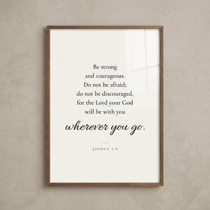 Studio hero shot of Joshua 1:9 'Be Strong and Courageous' scripture print in warm walnut wood frame on greige limewashed plaster wall with subtle realistic glass reflection. Modern minimalist Christian wall art instant download, perfect Father's Day gift, Christian dad present, confirmation, graduation, baptism keepsake.