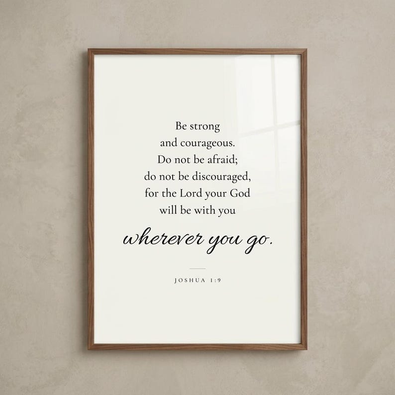 Studio hero shot of Joshua 1:9 'Be Strong and Courageous' scripture print in warm walnut wood frame on greige limewashed plaster wall with subtle realistic glass reflection. Modern minimalist Christian wall art instant download, perfect Father's Day gift, Christian dad present, confirmation, graduation, baptism keepsake.