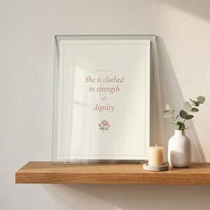 She Is Clothed in Strength and Dignity Proverbs 31 25 Wall Art Coquette Christia — room setting mockup in cozy living space with complementary decor. This coquette bow, botanical, pink blush christian scripture wall art print features beautiful serif typography on warm cream background. Proverbs 31 25 bible verse digital download printable for home office bedroom living room gallery wall decor....