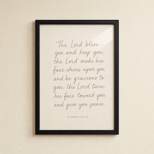 Front-on view of the Numbers 6:24-26 priestly blessing print in a slim matte black wood frame on a clean cream plaster wall, soft glass reflection visible. Hand-lettered terracotta Aaronic blessing typography for modern Christian wedding scripture wall art, instant digital download.