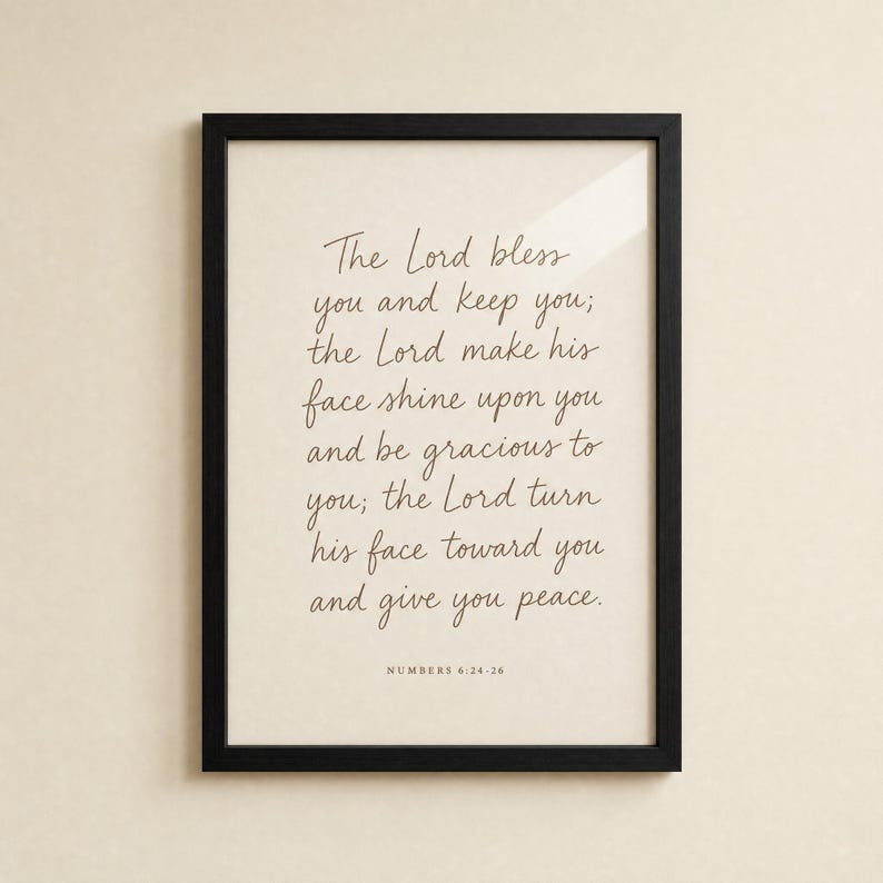 Front-on view of the Numbers 6:24-26 priestly blessing print in a slim matte black wood frame on a clean cream plaster wall, soft glass reflection visible. Hand-lettered terracotta Aaronic blessing typography for modern Christian wedding scripture wall art, instant digital download.
