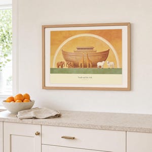 Kitchen mockup of Noah and the Ark framed in light oak above a pale stone counter, white cabinetry, a linen cloth, and a bowl of oranges. The artwork shows a wooden ark beneath a rainbow with three animal pairs, elephants, giraffes, and sheep. Bright window light and the warm cream mat demonstrate how the Christian print works in a clean, welcoming kitchen interior.