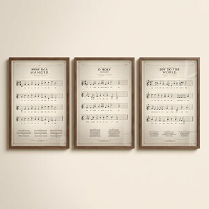 Christmas Hymns Gallery Wall Set of 3 vintage sheet music prints in solid walnut frames, frontal studio shot on cream backdrop, soft top-left key light, glass reflection visible, classical Christmas wall art digital download from TheFramedVerse — Away in a Manger, O Holy Night, Joy to the World hymnal page reproductions