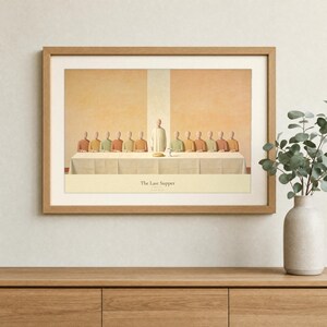 The Last Supper wall art in a light oak landscape frame hung above a cream linen sofa, terracotta vase with dried olive branches on a walnut console, warm plaster wall and soft afternoon daylight. Thirteen abstract faceless figures in terracotta, cream and olive earth tones share one long table. Modern Christian living room decor, Luke 22:19 printable download from TheFramedVerse on Etsy.