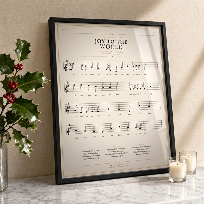 Joy to the World vintage sheet music print in a thin black wood frame on a white Carrara marble surface, a single holly branch with berries casting a soft shadow, two cream unlit votive candles, warm beige wall backdrop, bright winter light with glass reflection. Editorial still life Christmas carol hymn print digital download TheFramedVerse.