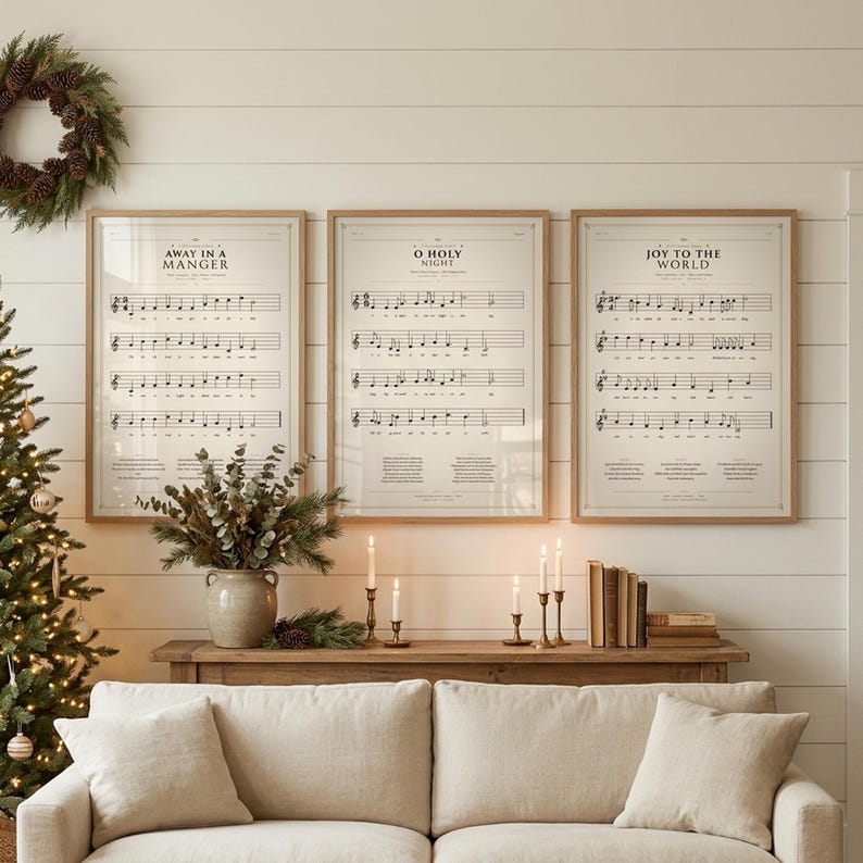 Christmas Hymns Gallery Wall Set of 3 vintage sheet music prints — Away in a Manger, O Holy Night, Joy to the World — displayed in light oak frames above a wooden console in a cozy farmhouse living room, decorated Christmas tree, brass candlesticks, eucalyptus and a pinecone wreath, warm holiday candlelight, classical christian wall art digital download from TheFramedVerse