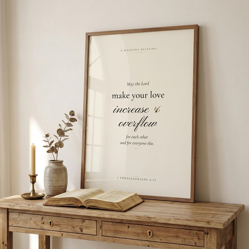 1 Thessalonians 3:12 Christian wedding scripture print framed in rustic walnut wood, leaning on a cream console next to an open vintage Bible, brass candlestick with lit beeswax candle, terracotta vase with dried wheat and white roses, cottage editorial newlywed Christian-faith home decor, TheFramedVerse digital download