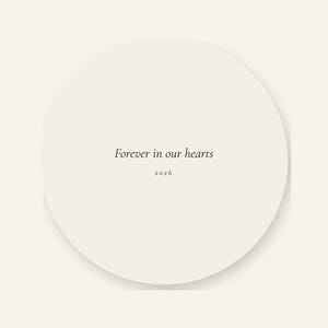 Back product card showing the reverse side of the double sided First Christmas in Heaven ornament against a warm cream background. The round acrylic keepsake displays the message Forever in our hearts in elegant script with the year 2026 below. A soft shadow and clean presentation make the coordinated back design and smooth circular shape easy to see.