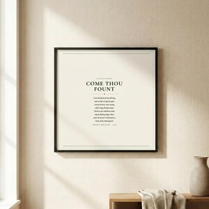 Come Thou Fount of Every Blessing christian hymn art print in thin black frame with white mat on warm cream linen wall, soft natural window light and gentle shadow, dark forest green Cormorant Garamond serif typography on cream, minimalist hymn lyric wall art hero product shot baptism confirmation gift