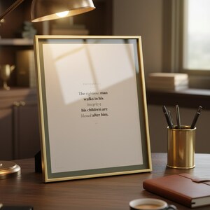 Proverbs 20:7 scripture wall art in gold glass frame sitting on dark wood masculine home office desk with warm brass desk lamp leather notebook and brass pen holder. Close up angle showing glass reflection. The righteous man walks in his integrity children are blessed. Sage green Father Day Christian gift for dad husband pastor digital download printable bible verse for study office bedroom decor