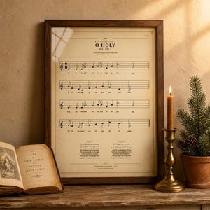 O Holy Night vintage hymnal print in a rustic walnut frame leaning on an antique console, an open vintage hymnal book beside it, a brass candlestick with beeswax candle, a sprig of holly and a dried orange slice, warm golden light. Cottage Christmas faith home decor, single classical carol hymn print digital download TheFramedVerse.