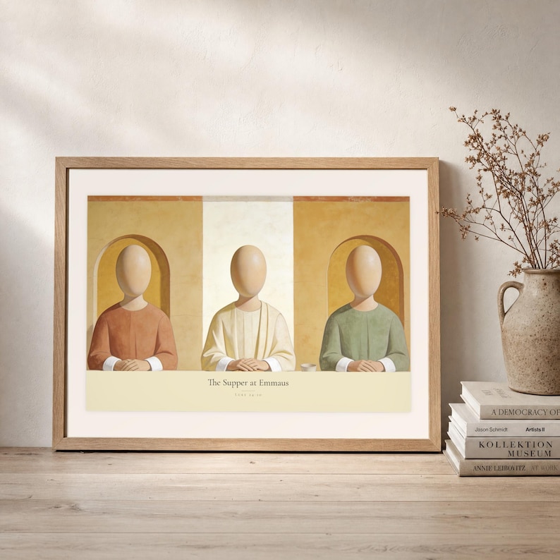 Leaning frame mockup of The Supper at Emmaus on a rustic wood console beside stacked art books and a tall ceramic vessel with dried stems. The print shows Christ seated at the center of a supper table within warm rounded niches. The oak frame, broad cream mat, plaster wall, and soft side light create a relaxed display while keeping the title and Luke 24:30 legible.