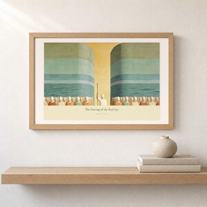 Shelf mockup of The Parting of the Red Sea in a light oak frame resting on a pale wood surface beside stacked neutral books and a rounded ceramic vase. The framed print shows Moses on the centre axis between two towering walls of water while the people cross the dry seabed. Cream matting, soft wall texture, and natural light present the horizontal Bible artwork at an easy domestic scale.