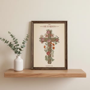 William Morris He is Risen Cross Print – Floral Easter Christian Decor, in vintage William Morris Arts and Crafts botanical style with ornate floral border on aged cream parchment, presented as a detailed front-facing mockup in a sleek black frame showing the complete William Morris botanical design with its rich colors and intricate patterns