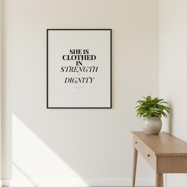 Proverbs 31 25 Wall Art She is Clothed in Strength and Dignity Scripture Print, — "She is clothed with strength and dignity, and she laughs without fear of the future", in elegant Mother's Day design with soft pink watercolor botanical flowers and graceful serif typography, photographed in beautiful close-up detail showing the premium glass frame reflection