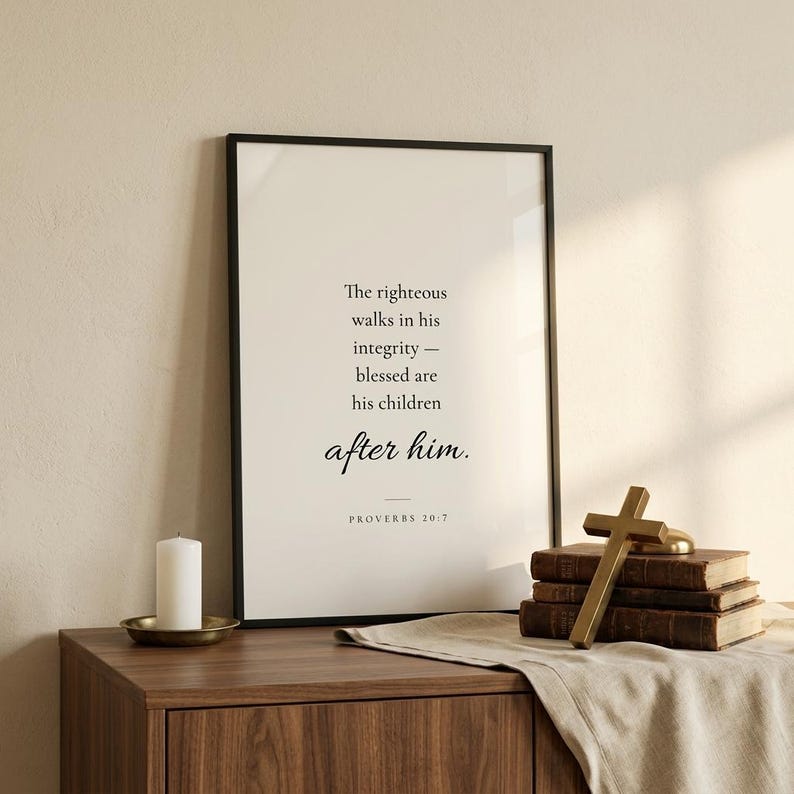 Proverbs 20:7 'The Righteous Walks in Integrity' in matte black frame leaning on walnut credenza beside a leather Bible stack, brass cross paperweight, and cream pillar candle. Classic Christian home interior styling. Father's Day gift for Christian dads, pastor appreciation, men's ministry print, instant download.