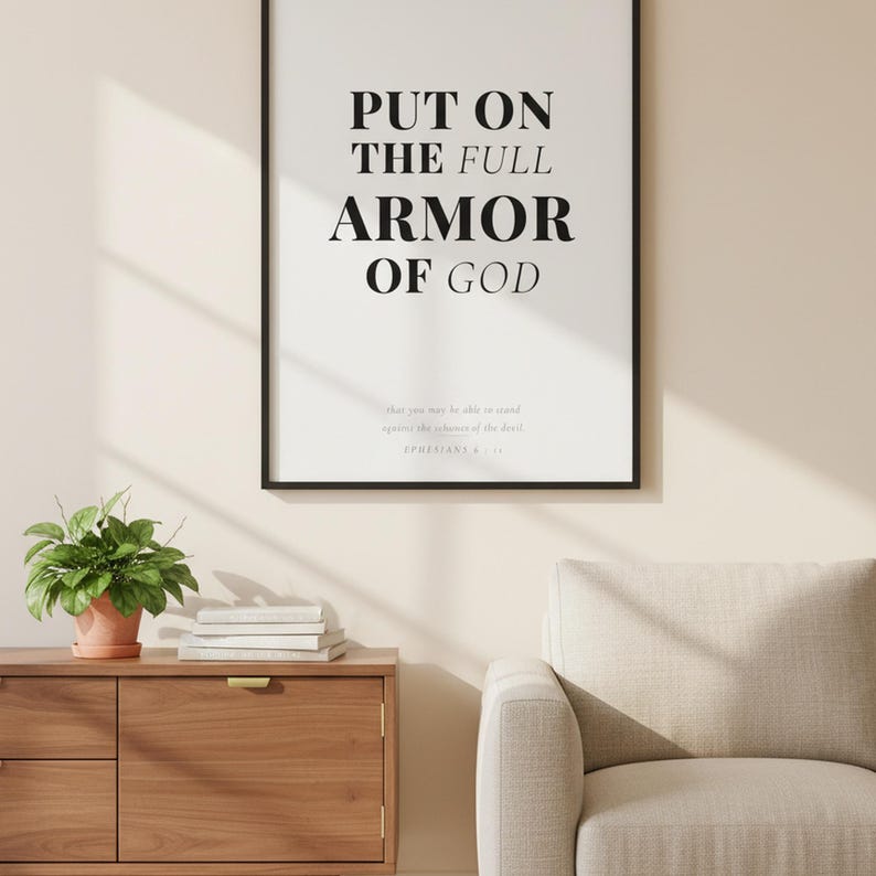 Ephesians 6 Wall Art Put on the Full Armor of God Scripture Print Christian Boys, — "Put on the full armor of God so that you can take your stand against the devil's schemes", in contemporary bold serif typography in black on clean white background, displayed in a beautifully styled modern living room above a warm wooden sideboard with soft natural light creating gentle shadows on the frame