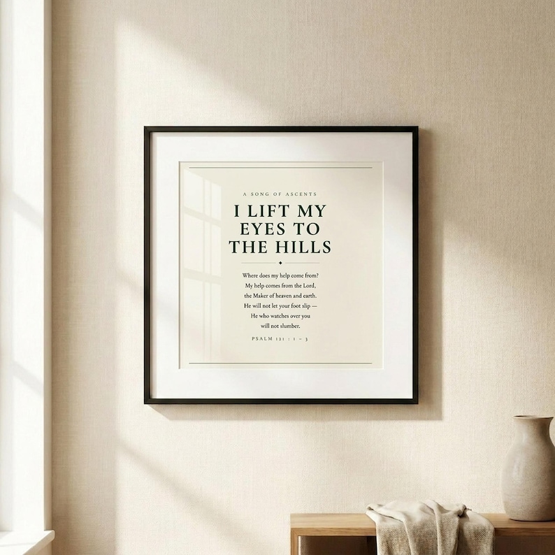Psalm 121 I Lift My Eyes to the Hills christian scripture art print in thin black frame with white mat on warm cream linen textured wall, soft natural window light and gentle shadow, dark forest green Cormorant Garamond serif typography on warm cream background, minimalist psalm 121 wall art hero shot baptism housewarming