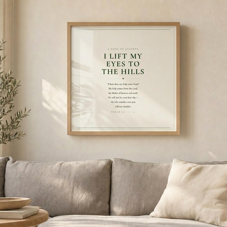 Psalm 121 I Lift My Eyes to the Hills scripture wall art print displayed above grey linen sofa in bright airy living room with olive branch in vase and palm leaf shadow, light oak wood frame, natural window light, christian minimalist home decor psalm 121 print baptism gift housewarming gift new home