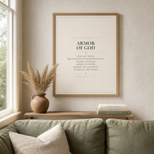 Warm lifestyle room with the framed design on a soft cream wall beside neutral decor and natural window light. The Armor of God artwork features Ephesians 6 in bold minimalist forest green typography on warm beige. This Armor of God print suits a boys room, confirmation gift, baptism, Sunday school space, or Christian bedroom as printable digital wall art.