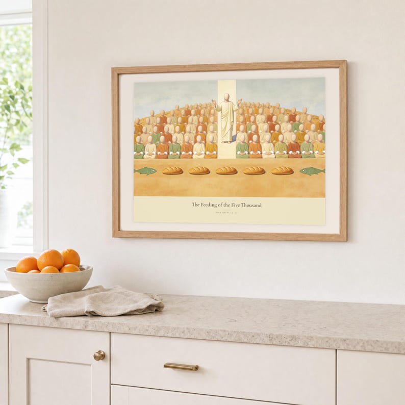 Kitchen mockup of The Feeding of the Five Thousand framed in light oak above a pale stone counter, white cabinetry, a linen cloth, and a bowl of oranges. The artwork shows Christ raised on the centre axis above a seated hillside crowd, with loaves and fish laid out along the foreground. Bright window light and the warm cream mat demonstrate how the Christian print works in a clean, welcoming kitchen interior.